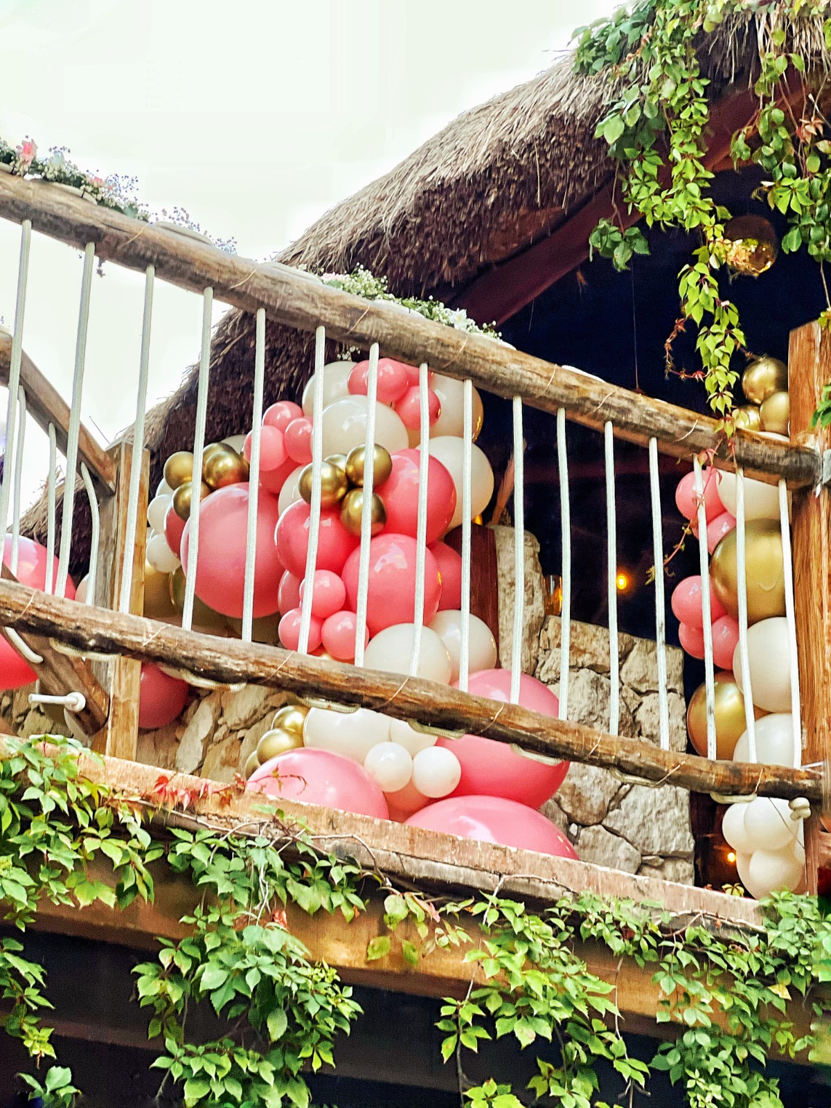 Pink, white and gold balloon garland along a wooden railing