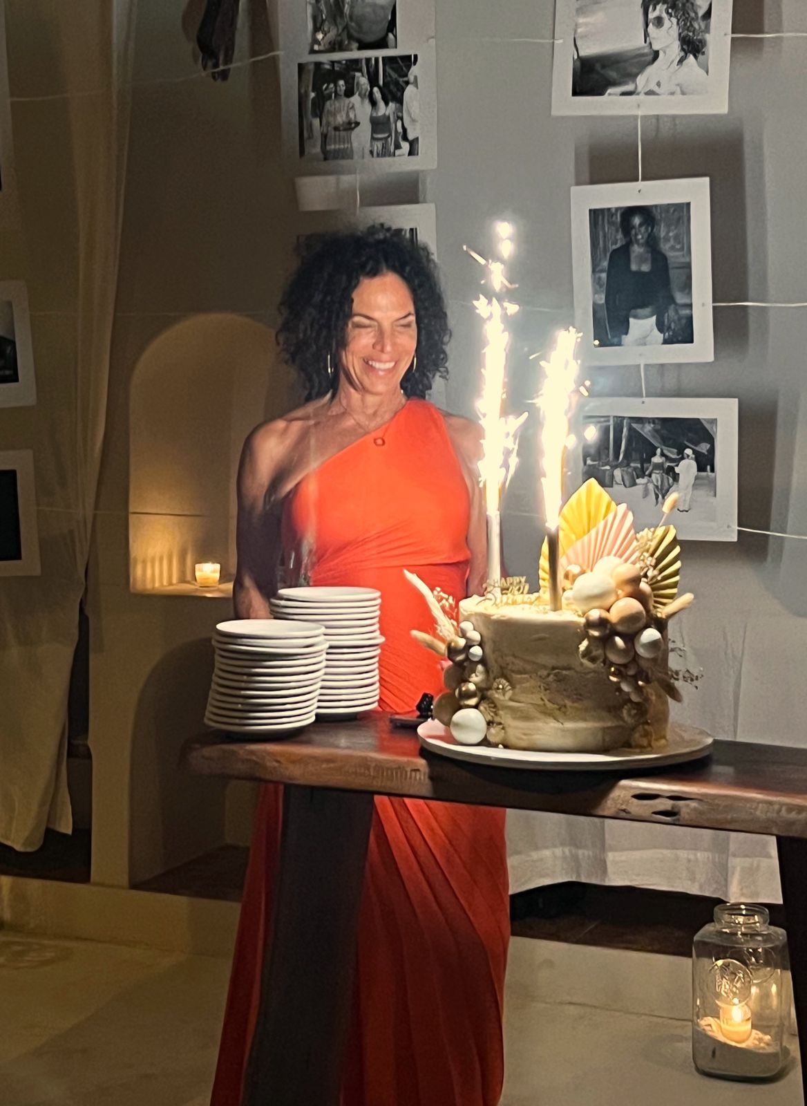 Woman in orange dress smiling beside a birthday cake with lit sparklers