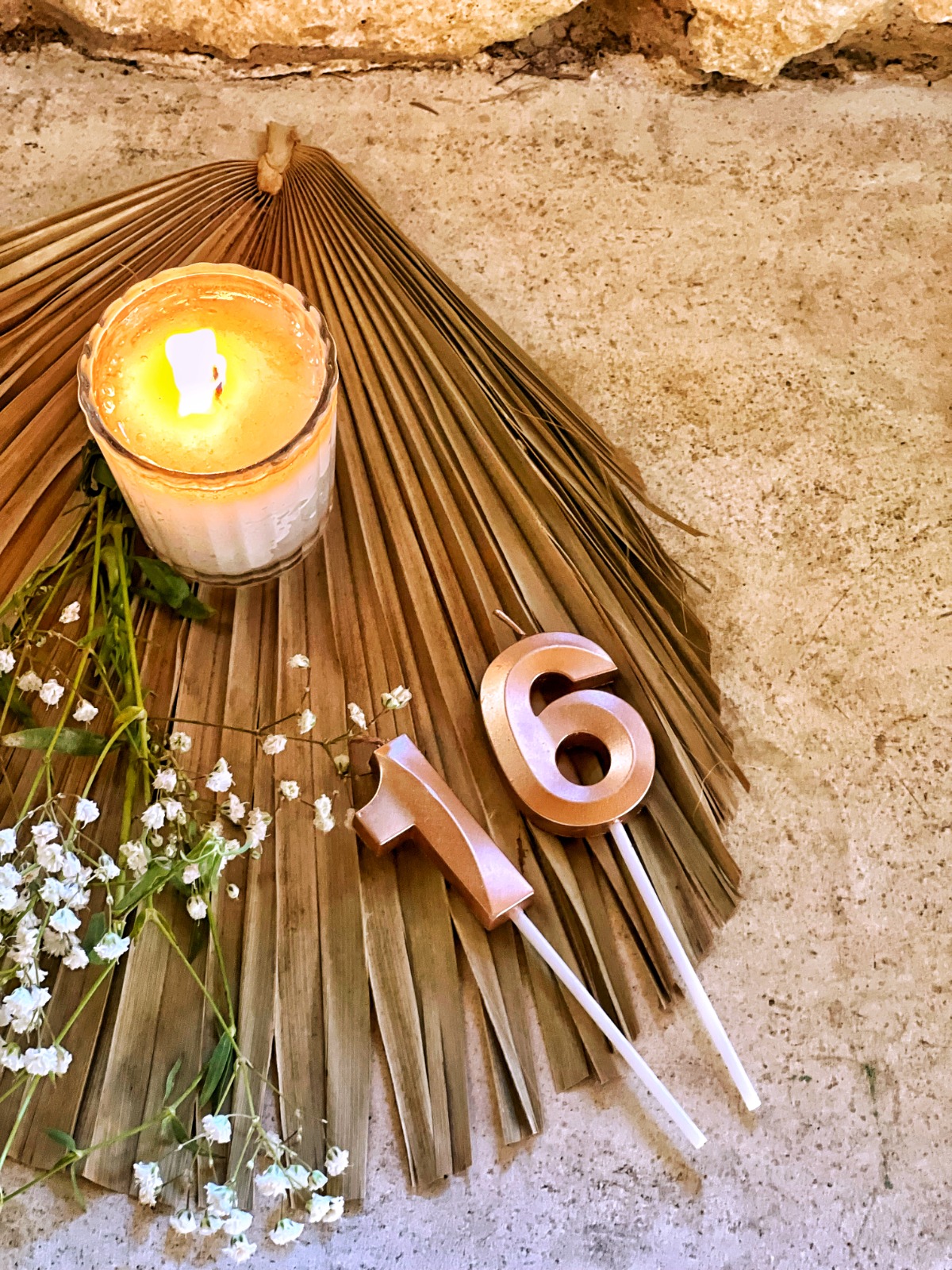 Rose gold number 16 birthday candles on a palm leaf