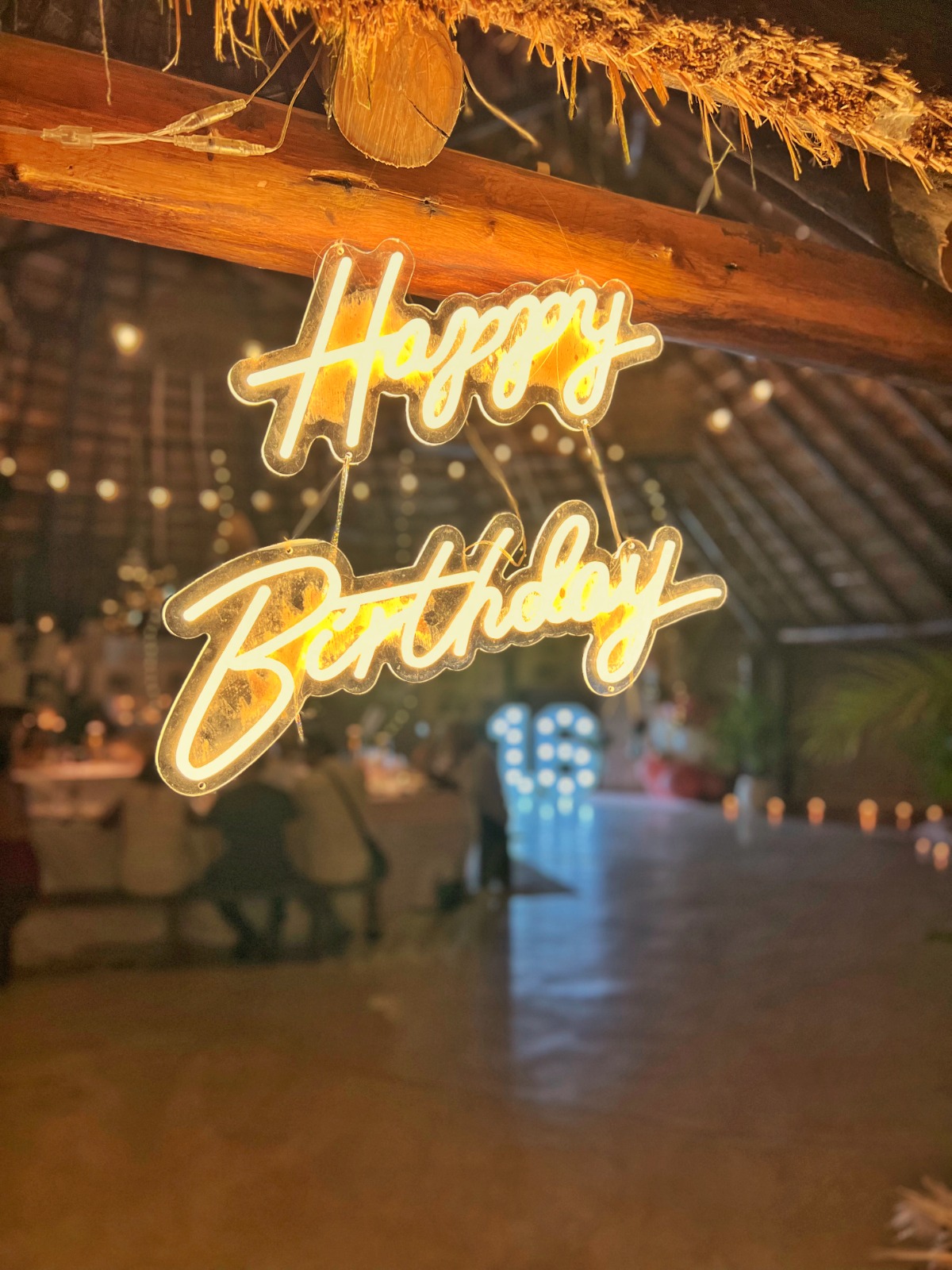 Hanging Happy Birthday neon sign under a palapa roof