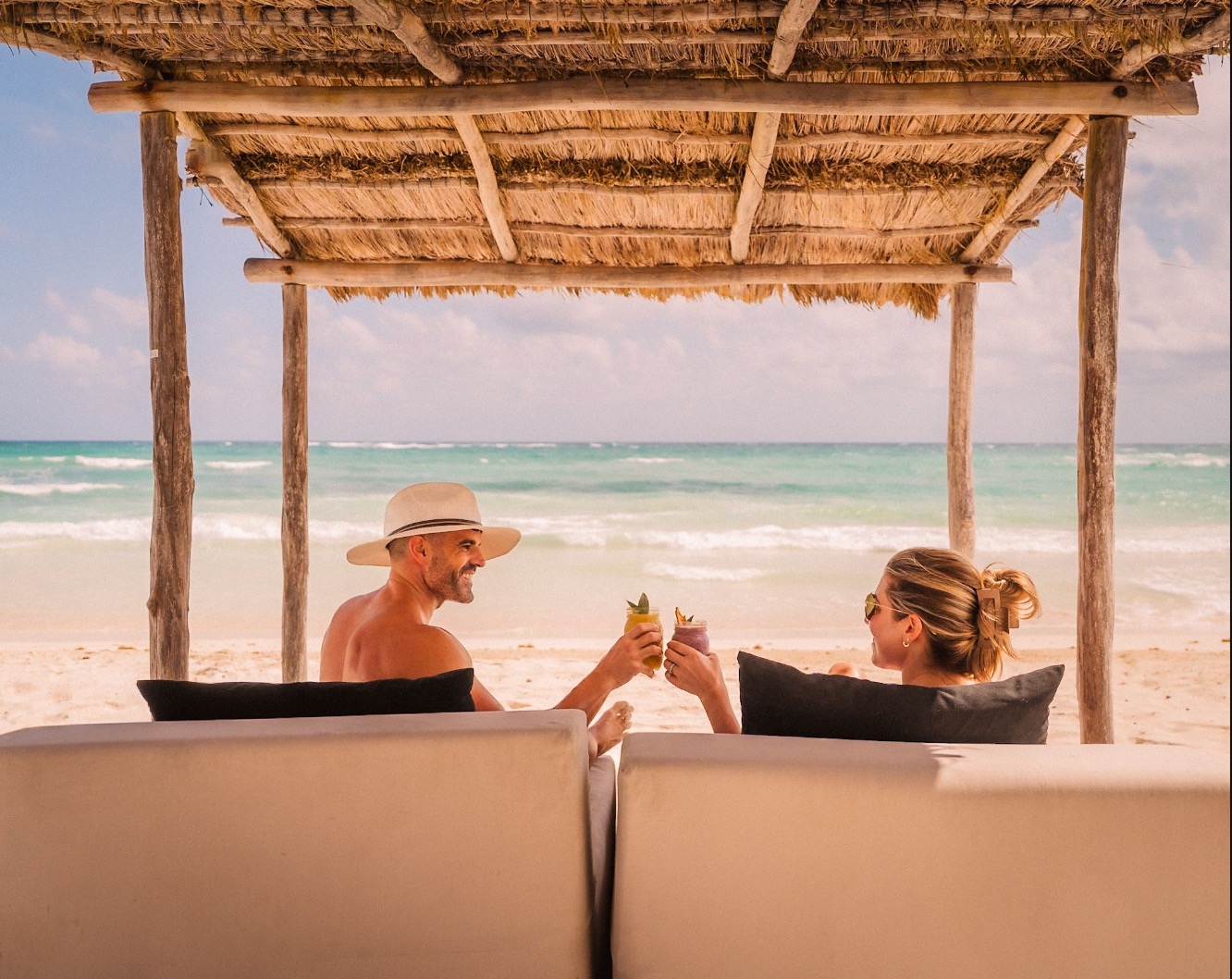 Couple relaxing with drinks under a palapa on the beach at Amansala, Tulum